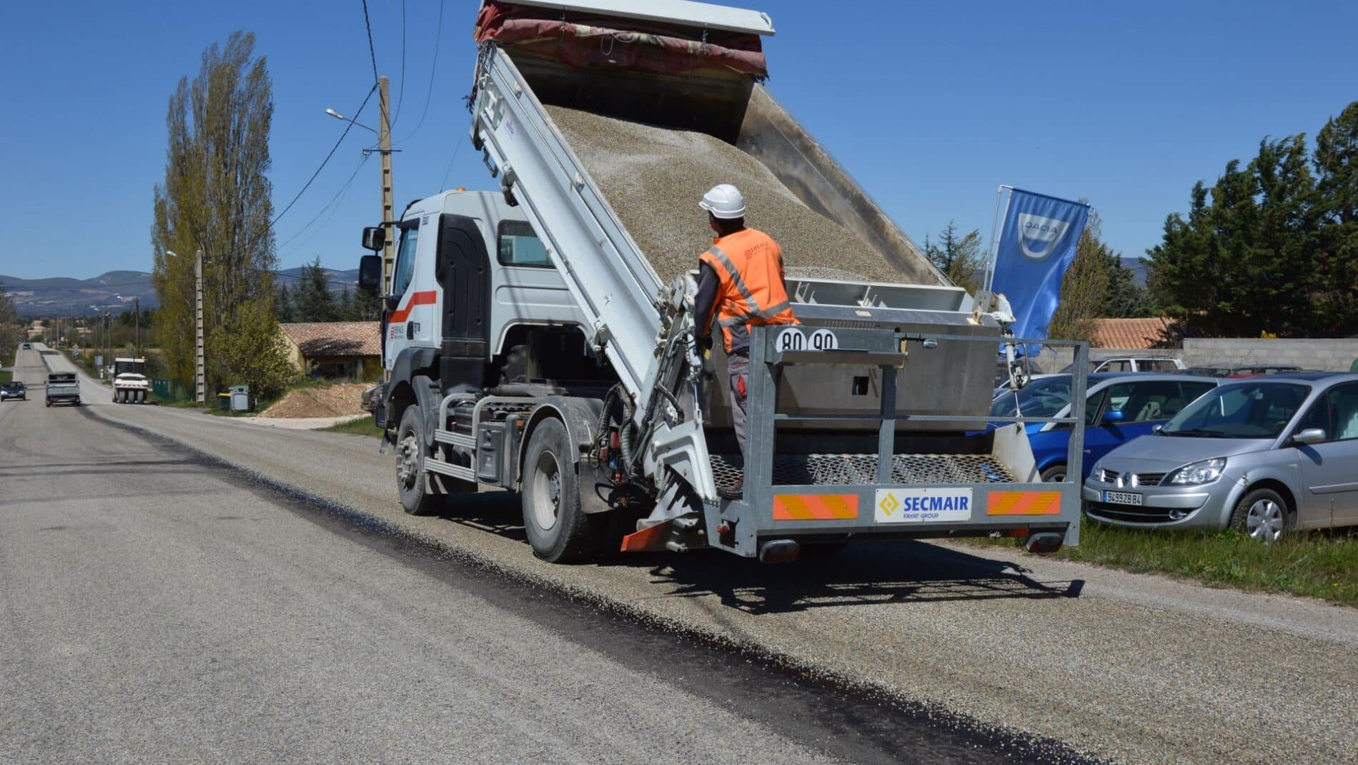 A dump truck unloading asphalt during road work with a worker in a reflective jacket.