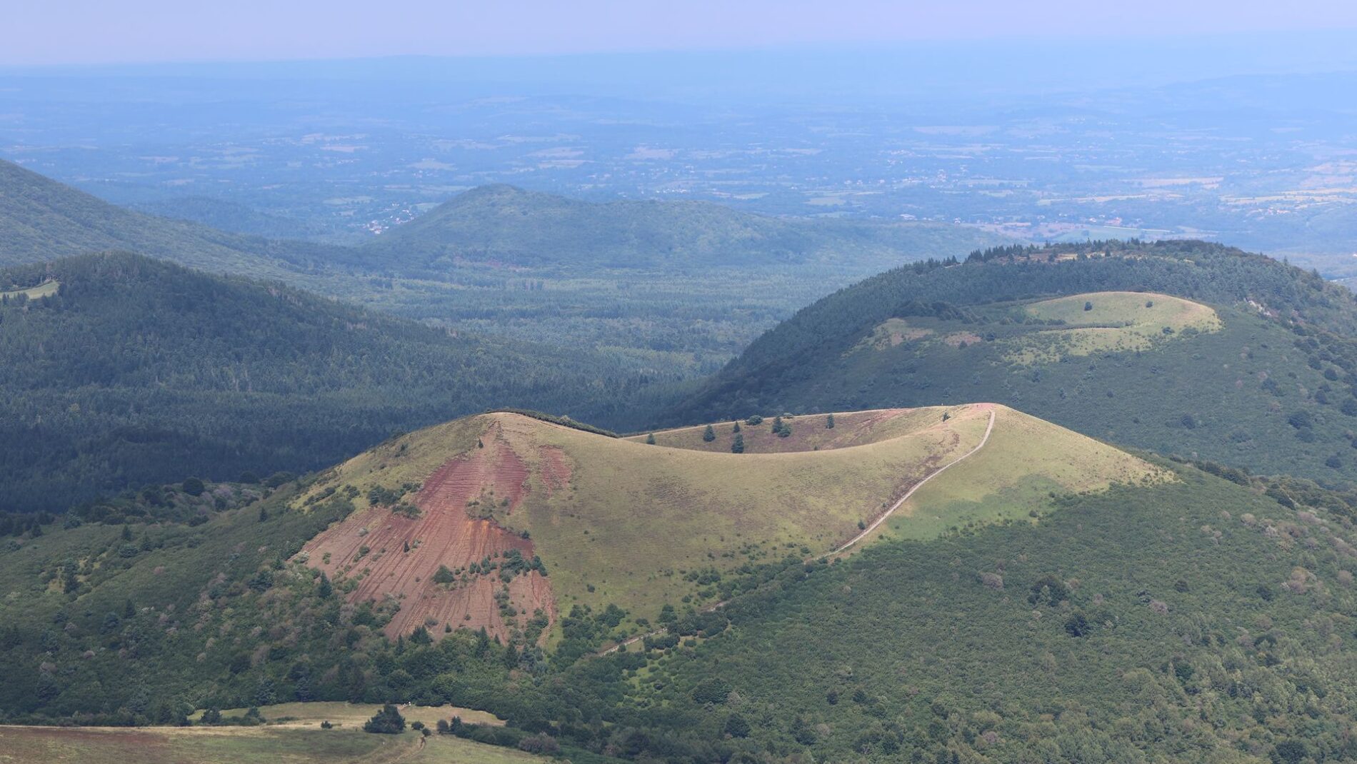 Stunning aerial view of volcanic hills in Auvergne, France, showcasing lush green landscape.