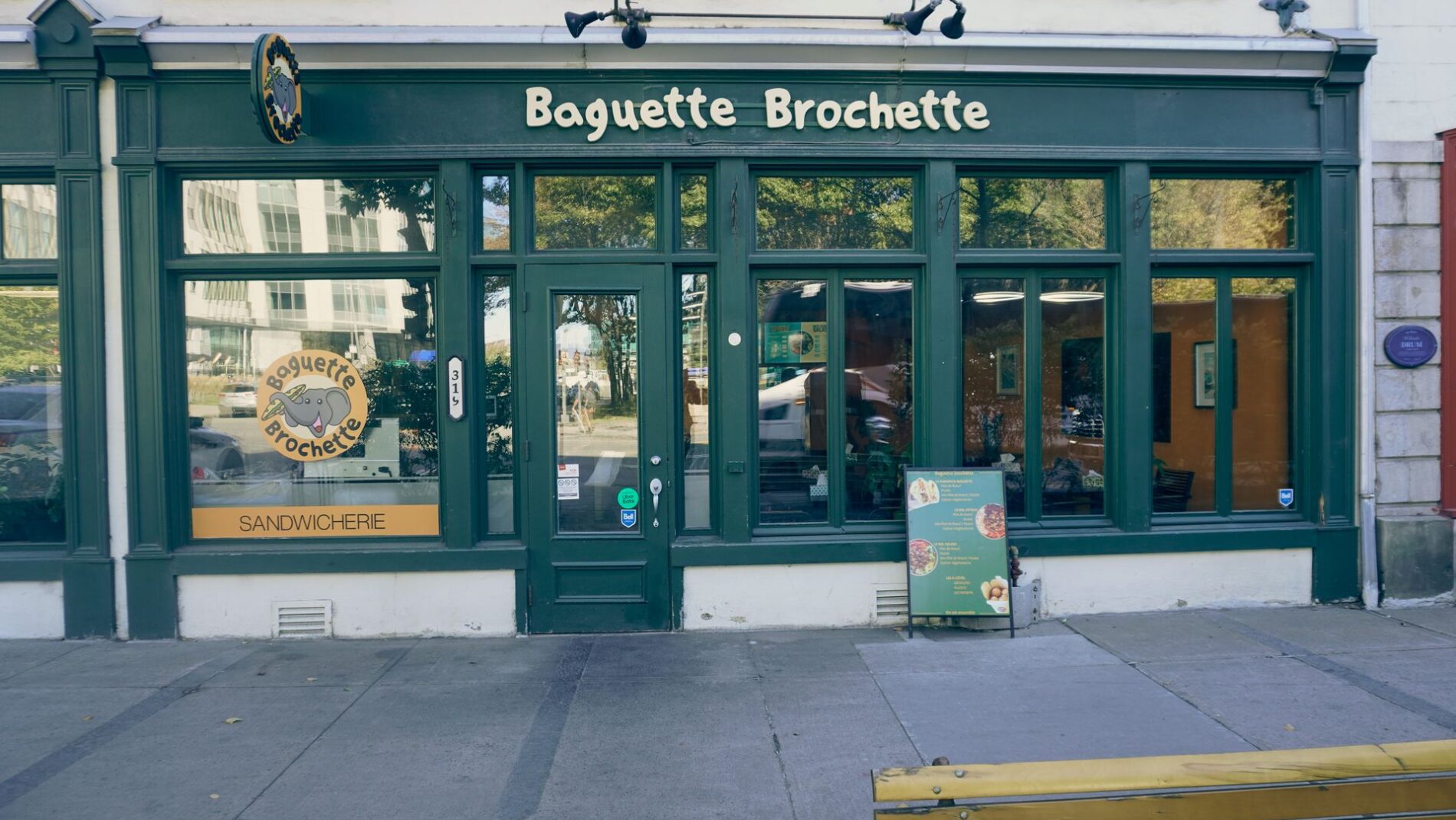 Charming street view of a French bakery called Baguette Brochette with green storefront and signage.