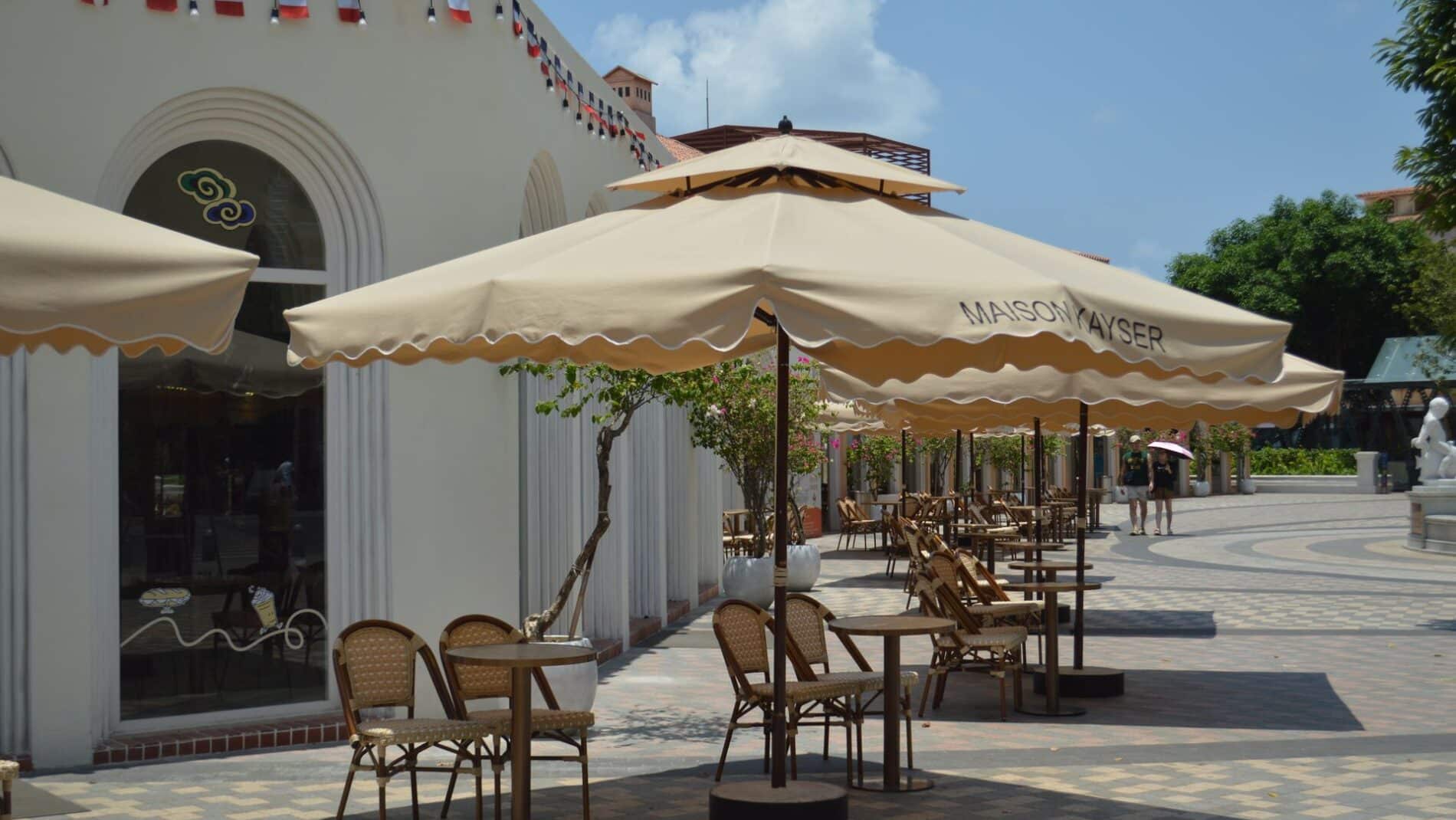 Charming outdoor cafe with tables, chairs, and beige umbrellas under a sunny sky.